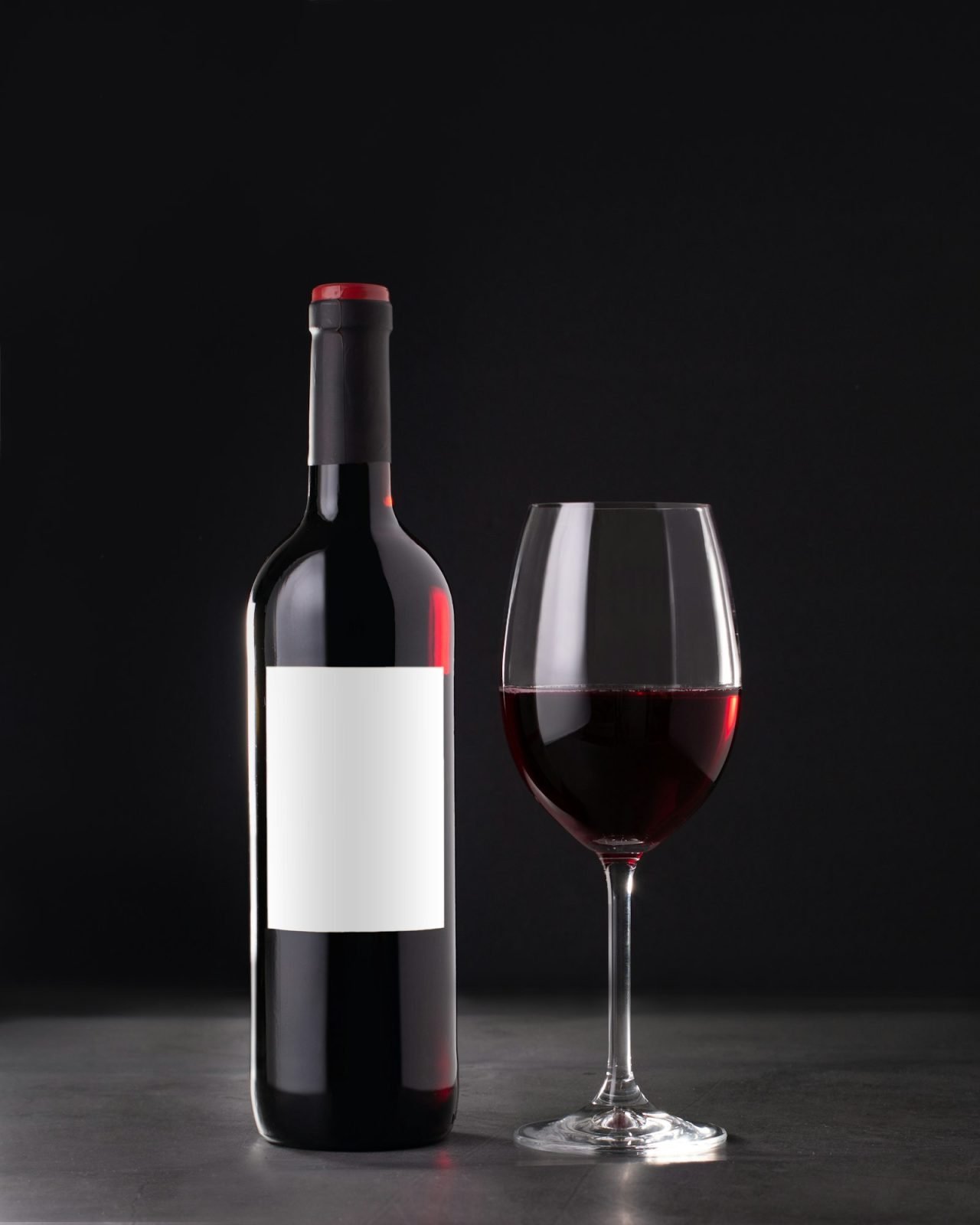 single red wine bottle with blank label for mockup and glass of red wine on dark gray background.jpg